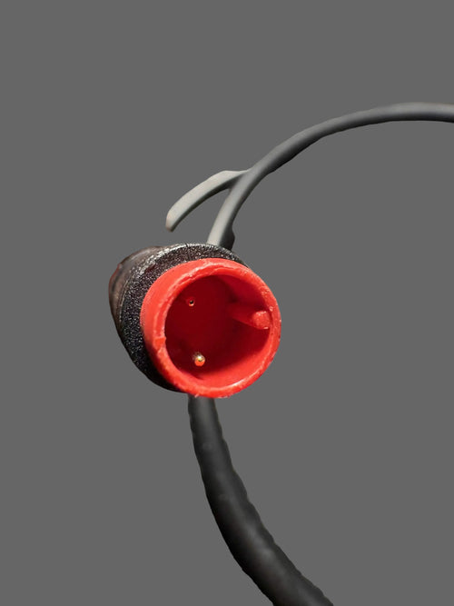 Black cable with a red connector held by a hand on a dark surface
